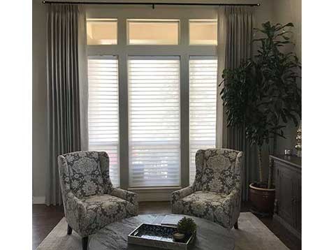 Living room with chairs and coffee table set in front of windows with Hunter Douglas shades.
